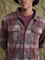 Sobrecamisa de tejido polar con estampado abstracto en tonos rojizos y azul marino. Presenta cuello clásico, cierre frontal con botones a presión, dos bolsillos frontales con solapa en el pecho y un parche decorativo.