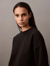 Buzo Calvin Klein de felpa francesa color negro, de corte holgado y diseño con cuello redondo. Cuenta con mangas largas, puños y dobladillo acanalados, y lleva el logo retro de la marca bordado discretamente en el pecho.