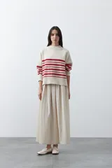 Polera de tejido de punto con diseño a rayas horizontales rojas sobre base color crema. Presenta cuello alto, mangas largas con puños acanalados y un corte holgado de silueta relajada.