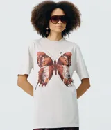 Remera oversized de algodón color gris claro, con cuello redondo y mangas cortas. Presenta una estampa frontal de mariposa marmolada en tonos tierra con pequeños detalles de strass.