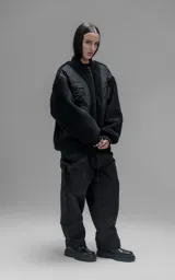Campera estilo bomber unisex, confeccionada en una combinación de corderito sintético y paneles de ripstop. Presenta un diseño utilitario con múltiples bolsillos frontales con cierres y broches a presión, cuello, puños y ruedo en ribb elástico.