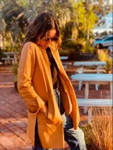 Tapado camel de cuero ovino con cuello clásico, cierre frontal con botones, bolsillos laterales y corte a la rodilla. Diseño slouchy y cómodo.