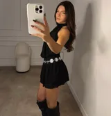 Vestido corto negro con escote halter, cintura elástica y falda con volados. Incluye un cinturón de cadena plateada con dijes redondos.