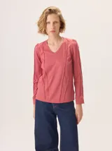 Remera de manga larga color rosado con cuello en V. Presenta detalles de costuras verticales tipo alforzas en el frente y hombros ligeramente fruncidos.