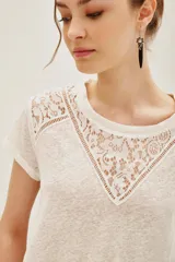 Remera de lino color blanco con detalle de encaje en el escote y hombros, de corte holgado y mangas cortas.