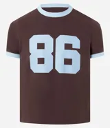Remera de algodón color marrón con cuello redondo y bordes de las mangas en color celeste. Presenta una estampa frontal con el número 86 en color celeste.