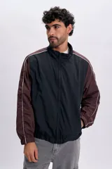 Campera estilo cortavientos en color azul oscuro, con mangas en tono marrón y detalles de líneas blancas en los hombros y mangas. Cuenta con cuello alto, cierre frontal y puños elásticos.