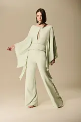 Pantalón sastrero verde claro, de corte amplio y recto, con detalles de apliques metálicos a lo largo de las costuras laterales.