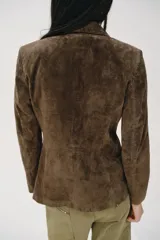 Blazer de ante color marrón, con cuello solapa, hombreras, manga larga y cierre frontal cruzado con botones. Cuenta con bolsillos delanteros de doble vivo.