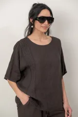 Blusa de lino color marrón oscuro, con escote redondo, mangas cortas amplias y detalle de alforzas verticales en el lateral derecho.