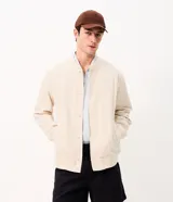 Campera bomber masculina de terciopelo cotelé color beige, con cuello redondo, mangas largas, cierre frontal de botones forrados, bolsillos laterales y terminaciones de elástico en puños y cintura.