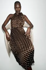 Vestido midi de color marrón con estampado de lunares blancos, cuello halter con lazo y diseño plisado.
