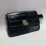 Tarjetero pequeño negro con textura de cocodrilo, cierre con broche metálico y gancho metálico para colgar.