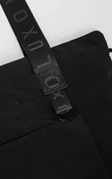 Tote bag negra de microfibra de alta densidad con diseño funcional. Presenta tiras de cinta de seguridad con logo grabado, sistema de elásticos laterales regulables para ajustar la silueta, bolsillo externo frontal con cierre y argolla metálica lateral.