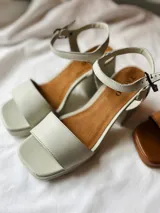 Sandalias de cuero color gris claro con taco cuadrado y tobillera ajustable.