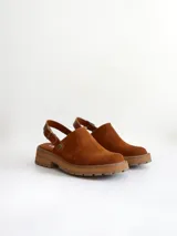 Zueco de cuero gamuzado color óxido, con tira trasera ajustable mediante hebilla metálica. Presenta una suela de plataforma con textura acanalada y detalle de textura reptil en la tira posterior.