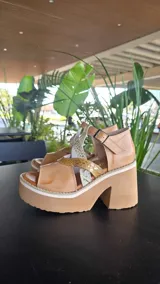 Sandalias de cuero color suela, con plataforma alta y taco ancho. Diseño con tiras cruzadas y apliques en texturas metalizadas y animal print, cierre con hebilla en el tobillo.