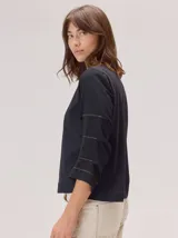 Remera de algodón color blanco, con cuello redondo y mangas tres cuartos con volados escalonados y detalles de pespuntes.