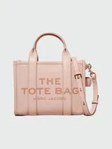 Cartera tipo tote de cuero granulado en color rosado, con diseño estructurado y asas superiores fijas. Incluye una correa ajustable y extraíble para llevar al hombro o cruzada. Presenta el logo de la marca y la inscripción 'THE TOTE BAG' grabados en el frente.
