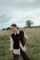 Chaleco de punto en color marrón oscuro, con cuello redondo y cierre frontal mediante botones metálicos decorativos con forma de sol.