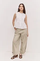 Blusa sin mangas de color blanco, con cuello redondo fruncido y cierre frontal de botones. Combina un cuerpo texturizado con una parte inferior de encaje calado y diseño peplum.