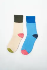 Par de medias de caña media con diseño color block. Una media es color crema con puntera verde y talón rosa, la otra es celeste con puntera rosa y talón azul marino.