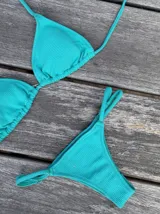 Conjunto de bikini color turquesa con tela acanalada. El corpiño es de triángulos ajustables con almohadillas removibles. La bombacha es vedetina con tiras regulables a los costados mediante hebillas.