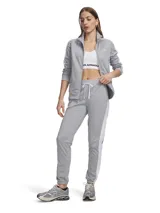 Conjunto deportivo Under Armour de tricot gris, compuesto por una campera con cierre frontal y cuello alto, y un pantalón de jogging con cordón ajustable en la cintura y franjas blancas laterales.