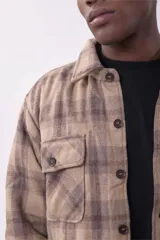 Campera tipo sobrecamisa de franela con diseño a cuadros en tonos beige y marrón. Presenta cuello clásico, cierre frontal con botones, dos bolsillos frontales con solapa y botones en el pecho, y mangas largas con puños abotonados.