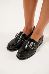 Mocasines negros de charol arrugado con horma redondeada y detalle de presilla con hebilla y ojalillos.