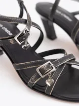 Sandalias de cuero vacuno en color tostado, con tiras múltiples en la capellada, doble hebilla con dijes colgantes, talón destalonado con tira ajustable y taco geométrico en color verde lima.