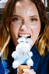 Llavero de peluche con forma de conejo blanco, con anteojos de sol en forma de corazón, vestido con un jardinero de tejido celeste y botones decorativos. Incluye una correa de cuerda trenzada multicolor y un dije de esfera a rayas.