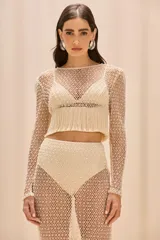 Blusa de malla color beige con bordado de perlas, mangas largas, corte ajustado y flecos en el bajo. Incluye un top de lycra como forro.