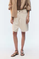 Bermuda de denim color blanco roto, de corte oversize y relaxed fit, con diseño de cinco bolsillos y terminación deshilachada en el ruedo.