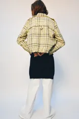 Chaqueta de corte recto confeccionada en tejido con textura de cuadros en tonos amarillos, blancos y negros. Presenta cuello solapa, cierre frontal con botones ocultos, bolsillos de plastrón con solapa en el delantero y mangas largas con puños abotonados.