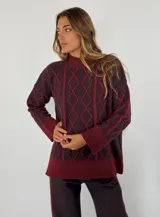 Sweater de lana color bordó con cuello alto y diseño de rombos y líneas verticales en rojo. Tiene puños y dobladillo acanalados.