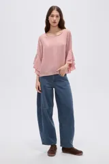 Blusa de poliéster color rosado, de diseño holgado, con cuello a la base y mangas 3/4 adornadas con volados escalonados.