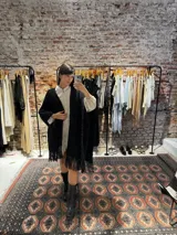 Ruana tejida a mano en lana merino color negro con sutiles detalles de brillos y terminación de flecos en el ruedo.