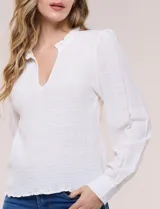 Blusa negra de silueta semi entallada confeccionada en rayón. Presenta un escote en V pronunciado con cuello mao fruncido, pechera con textura elástica en punto smock, mangas largas fluidas con frunces en los hombros y puños anchos.