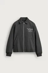 Cazadora gris oscura de corte relaxed fit con patrón de rayas diplomáticas. Confeccionada con tejido de lana, presenta cuello camisero, cierre frontal de cremallera metálica, bolsillos de vivo en la cadera, puños y dobladillo elásticos, y un delicado bordado de texto a contraste en el pecho.