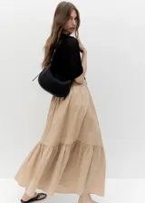 Riñonera de diseño minimalista en color negro, confeccionada en material efecto piel con acabado liso. Presenta una forma curva estructurada, cierre superior con cremallera y una correa ajustable con hebilla metálica que permite llevarla al hombro o cruzada.