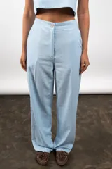 Pantalón de lino color celeste, de corte recto y tiro alto, con cierre frontal de botón y cremallera.