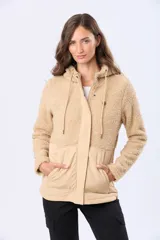 Campera beige con capucha y cordones ajustables, combinada en su parte superior con tejido de corderito y en su parte inferior con diseño capitoné. Cuenta con cierre frontal y broches a presión, además de bolsillos laterales.