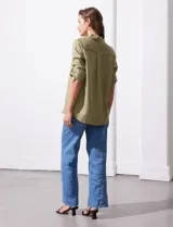 Camisa color verde oliva de lyocell, marca Cyrus. Tiene cuello con solapa, abertura central con botones, mangas 3/4 regulables con presilla y botón, y dos bolsillos delanteros aplicados.