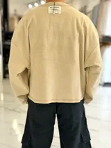 Buzo oversize color beige, con costuras externas visibles y gran estampado tipográfico y gráfico en la espalda.