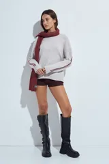 Sweater gris de calce relajado con cuello redondo y mangas largas. Presenta detalles de rayas horizontales en color rojo a lo largo de las mangas, con puños y ruedo acanalados.