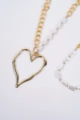 Set de dos collares plateados. Uno de ellos presenta una cadena de eslabones combinada con perlas irregulares y un dije grande en forma de corazón. El otro collar es una gargantilla de perlas irregulares con una sección de cadena de eslabones y cierre ajustable.