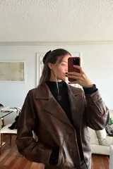 Campera bomber de cuero ovino en tono óxido, con diseño de solapas, cierre frontal con botones de guampa y detalles de pasamanería trenzada en las mangas.