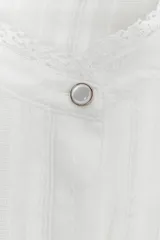 Blusa blanca de manga larga con cuello redondo, confeccionada con detalles de bordados y volantes a tono. Presenta cierre frontal con botones ocultos y puños ajustados.