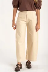 Pantalón de corte baggy y tiro medio, confeccionado en algodón peinado de color arena. Presenta diseño de pierna ancha, cierre frontal con botón y bolsillos laterales.